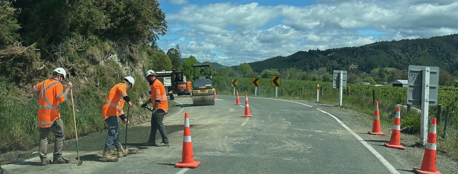 Road workers on a curving road resurfacing the seal