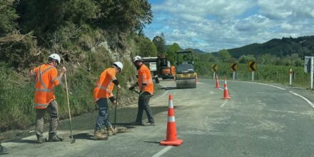 Road workers on a curving road resurfacing the seal