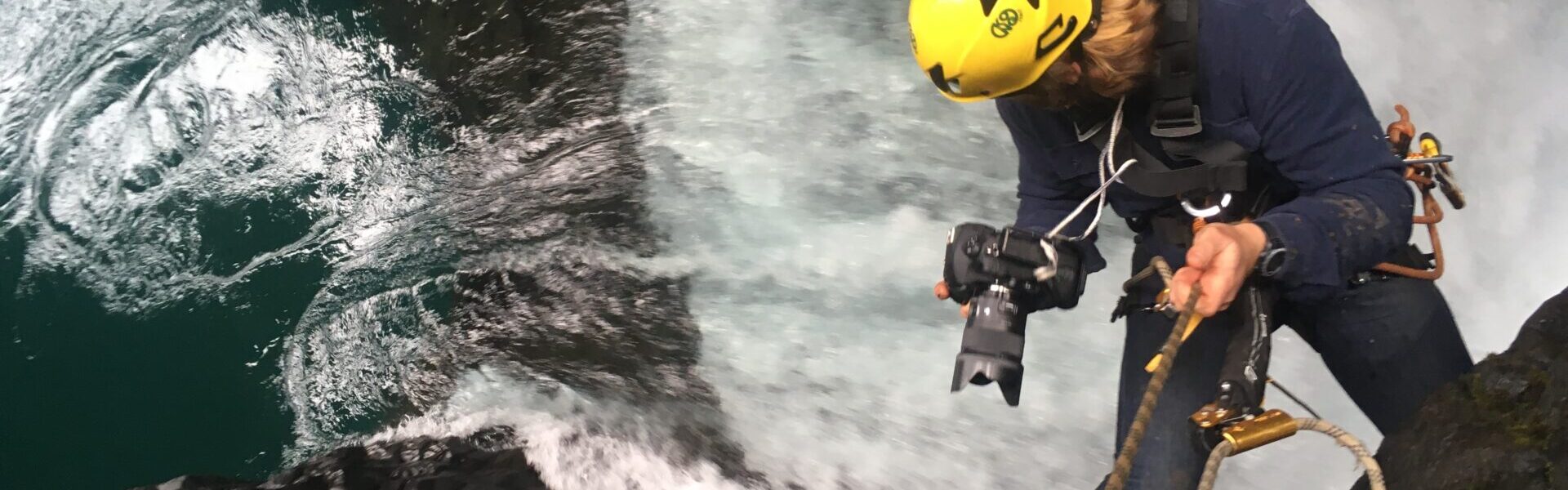 A man with a camera dangles from height above a river