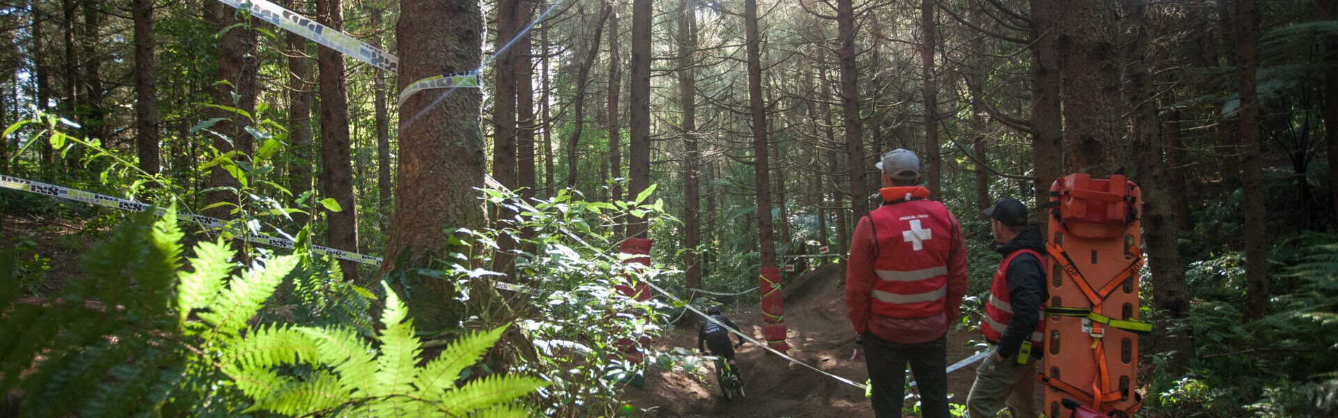 Two medics stand in the forest light overlooking a bike trail