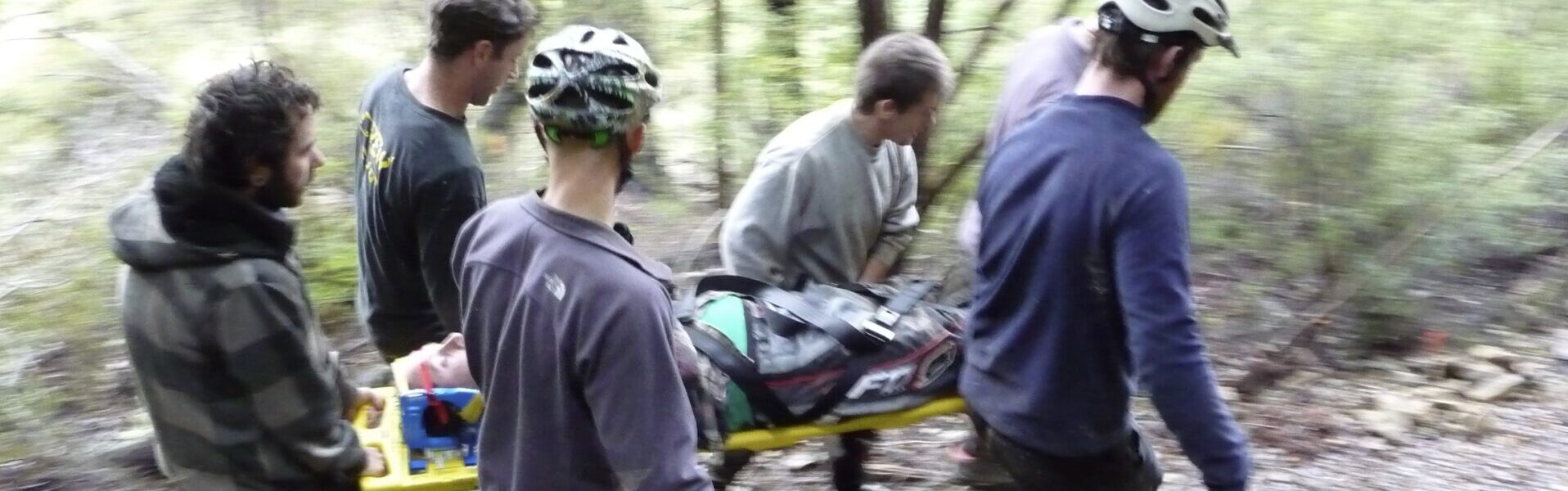 Group of people with helmets on carry a person lying on a backboard through the forest