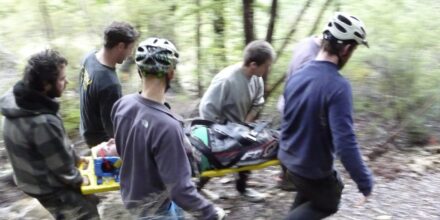 Group of people with helmets on carry a person lying on a backboard through the forest